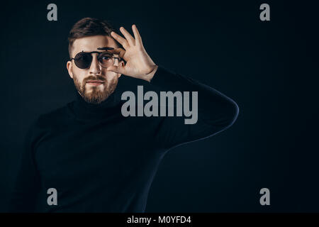 Portrait of handsome bearded man in black turtleneck looking at camera in flip sunglasses on black. Stock Photo