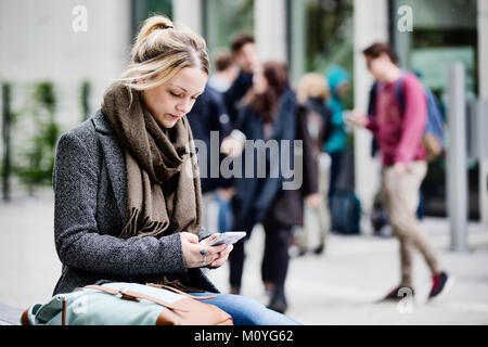 Young woman,student,sitting on campus with her smartphone,Cologne,North Rhine-Westphalia,Germany Stock Photo
