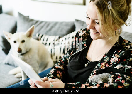 Young woman sits on the sofa with her dog and looks at a tablet computer,Germany Stock Photo