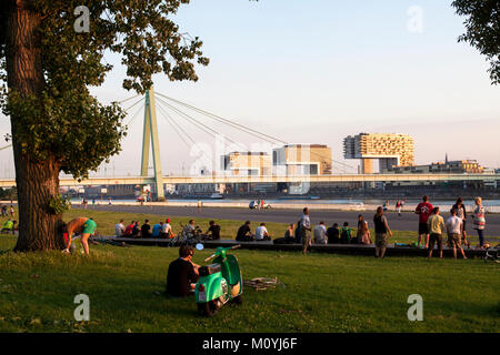 Germany, Cologne, people enjoying the summer evening at the banks of the river Rhine in the district Deutz, view to the Severins bridge and the harbor Stock Photo