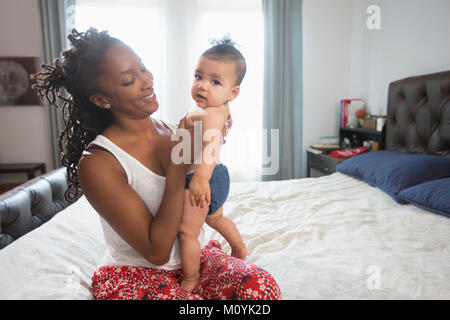 Mother sitting on bed holding baby daughter Stock Photo