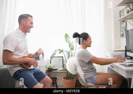 Man playing ukulele watching woman using computer Stock Photo