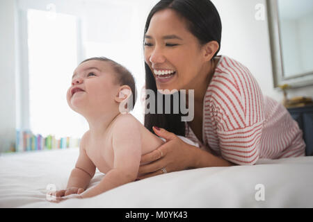 Mother playing with baby son laying on bed Stock Photo