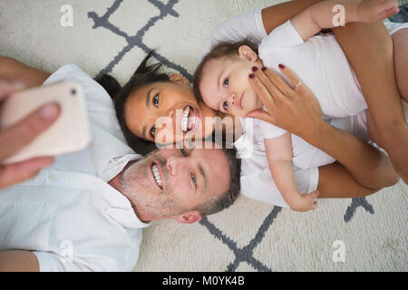 Family laying on floor posing for cell phone selfie Stock Photo