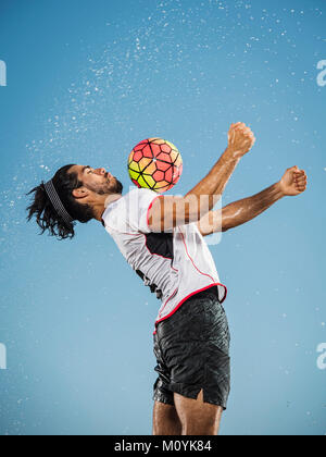 Water spraying on Hispanic man trapping soccer ball on chest Stock Photo