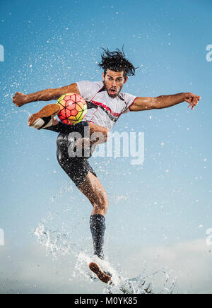 Water spraying on Hispanic man kicking soccer ball Stock Photo