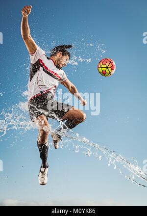 Water spraying on Hispanic man heading soccer ball Stock Photo