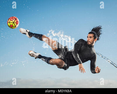 Water spraying on Hispanic man kicking soccer ball Stock Photo