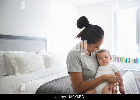 Mother holding baby son in lap on bed Stock Photo