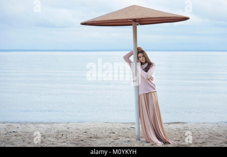 Pensive Caucasian woman leaning on beach umbrella Stock Photo