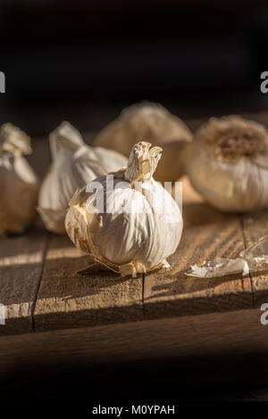 Several heads of fresh garlic on a wooden board with dark background in natural lighting Stock Photo