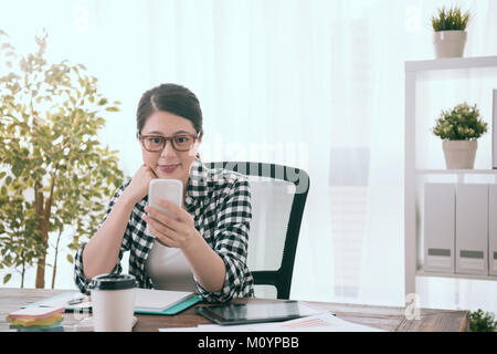 happy leisurely business woman finished working and sitting on workplace at home using mobile cell phone browsing online information relaxing. Stock Photo