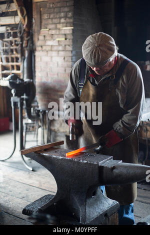 Blacksmith hammering molten metal to forge a horseshoe in Flett's Blacksmith Shop at Heritage Park Historical Village, Calgary, Alberta, Canada Stock Photo
