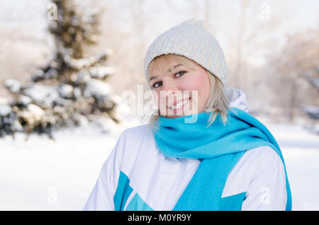 portrait of an attractive blonde smiling girl in a sports jacket and hat in a snowy forest. concept walks in the winter forest for health. Stock Photo