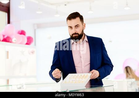 Attractive man with a beard showing a collection of wedding rings. Buying wedding ring. Customer service in jewelry store. Stock Photo