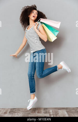 Caucasian brunette female in casual posing on camera with a lot of packages in hand, being satisfied after shopping over grey wall in studio Stock Photo