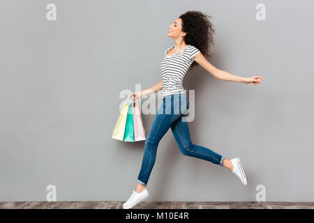 Happy emotions of wonderful female in jeans carrying a lot of purchases in hand, during shopping at sale day isolated in studio Stock Photo