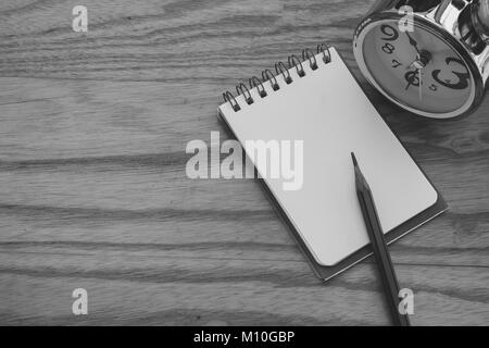 Business Creative and Idea Concept : Used pencil put on notebook with silver alarm clock put on wooden table in black and white image. Stock Photo