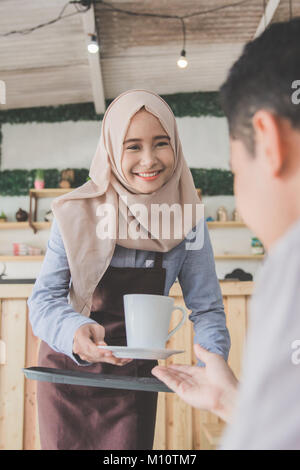 portrait of man sitting in cafe served with coffee by asian muslim female waitress Stock Photo