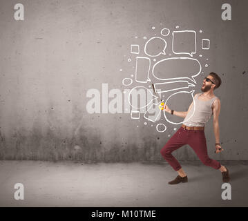 A comic hipster guy shouting in front of grey urban concrete wall with drawn empty text bubbles around his mouth concept Stock Photo