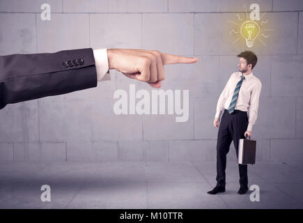 A huge ordering hand pointing at scared and confused businessman with a good idea illustrated by a drawn glowing light bulb concept Stock Photo