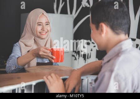 portrait of young man sitting in a cafe bar served with coffee by asian muslim female waitress Stock Photo