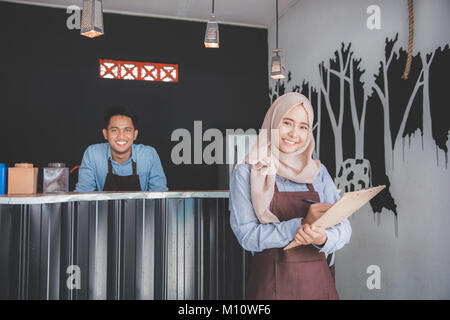 Happy asian male waiter using apron writing order. muslim entrepreneur concept Stock Photo