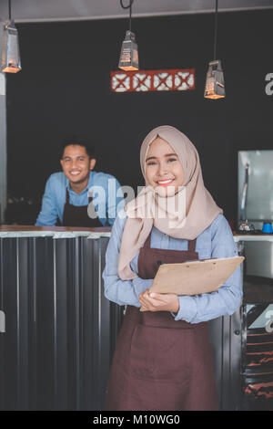 Happy asian male waiter using apron writing order. muslim entrepreneur concept Stock Photo