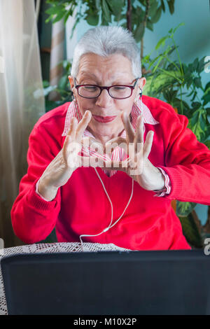 Grandma using laptop, camera and earphones for distant connections Stock Photo