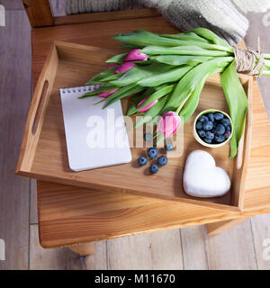 A tray with tea and gingerbread in the shape of heart and a bouquet of tulips on the chair Stock Photo