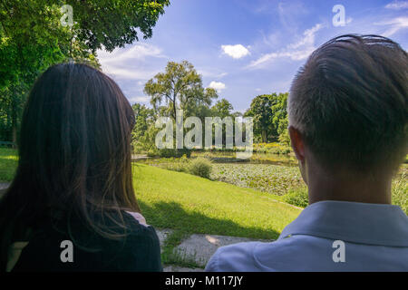 Young Couple from the back sitting together on a bench in the shadow. Stock Photo