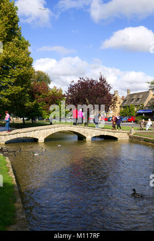 Bourton-on-the-Water, England - October 7th 2010: Visitors and tourists take advantage of the Autumn sunshine in 'The Venice of the Cotswolds' as Bourton-on-the-Water is sometimes called. The earliest of the five local stone bridges was built in 1654.  UK, Gloucestershire, Cotswolds, Bourton-on-the-Water. Tourists enjoying Autumn sunshine by the river. Stock Photo