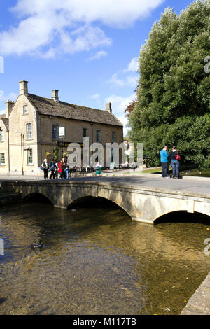 Bourton-on-the-Water, England - October 7th 2010: Visitors and tourists take advantage of the Autumn sunshine in 'The Venice of the Cotswolds' as Bourton-on-the-Water is sometimes called. The earliest of the five local stone bridges was built in 1654.  UK, Gloucestershire, Cotswolds, Bourton-on-the-Water. Tourists enjoying Autumn sunshine by the river. Stock Photo