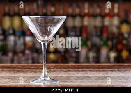 An empty martini glass stands on the bar in the restaurant, on a blurry background of alcohol Stock Photo