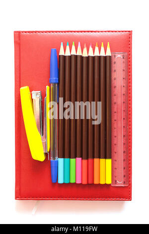 Yellow stapler, pen, ruler, colored pencils on a red diary Stock Photo