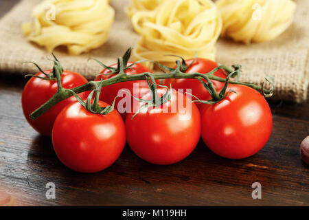 cherry tomatoes on a branch and raw tagliatelle paste in the background, on a wooden background Stock Photo