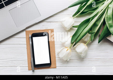empty phone screen and laptop and tulips on white wooden rustic background. stylish flat lay with flowers and working gadgets with space for text. fre Stock Photo