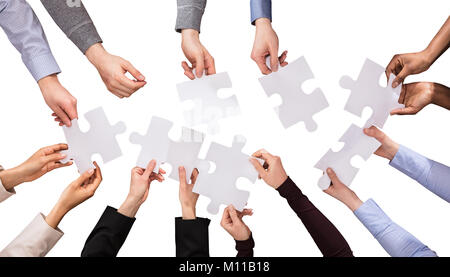 Elevated View Of Hands Holding White Jigsaw Puzzles Against White Background Stock Photo