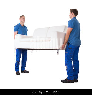 Two Young Movers Moving White Sofa In New Home Against White Background Stock Photo