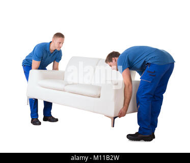 Young Professional Movers In Uniform Placing The Sofa In New Home Against White Background Stock Photo