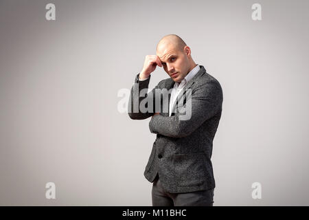 A young bald man in a gray suit and white shirt stands pensively and looks at the camera on a white isolated background Stock Photo