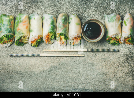 Helathy Asian cuisine. Flat-lay of vegan spring or summer rice paper rolls with vegetables, sauce and chopsticks over concrete background, top view, c Stock Photo