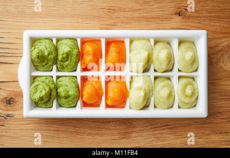 Pureed baby food in ice cube trays ready for freezing on wooden table, top view Stock Photo