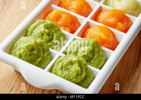 Pureed baby food in ice cube trays ready for freezing on wooden table Stock Photo