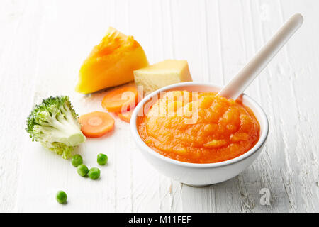 Pumpkin and carrot baby puree in bowl with baby spoon on white wooden table Stock Photo