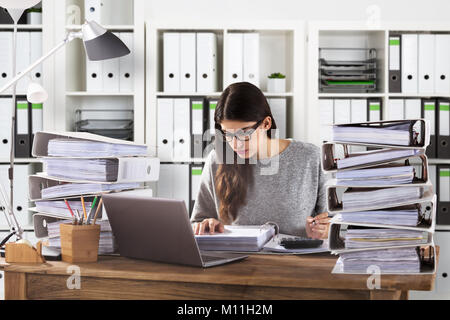 Young Businesswoman Wearing Eyeglasses Calculating Bill In Office Stock Photo