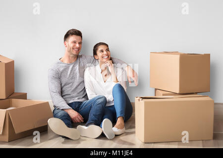 Happy Couple Sitting On Floor With Cardboard Boxes In Their New Home Stock Photo