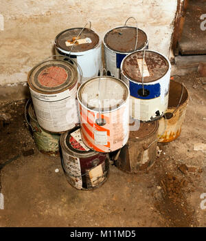 Empty stacked paint cans on dirty basement floor. Stock Photo
