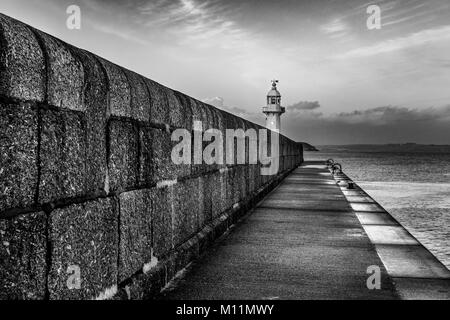 Monochrome representaion of Mevagisseys routinley battered, sea facing harbour wall protecting both the lighthouse and all manner of vessels within it Stock Photo