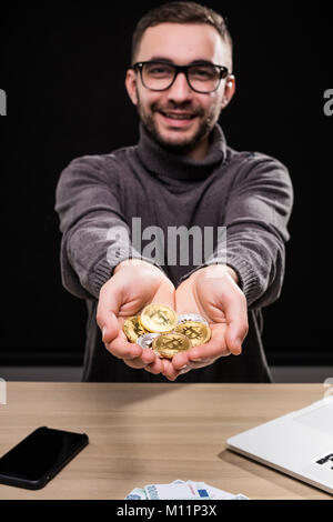Portrait of man in glasses showing golden bitcoins in his hands isolated over black background Stock Photo